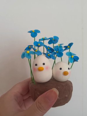 Two Adorable Clay Ducks Surrounded by Blue Flowers